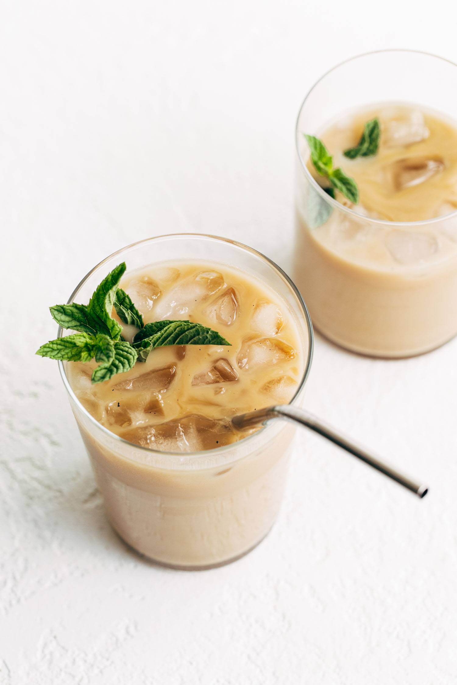 Café helado de vainilla y menta en dos vasos, uno con pajita de metal.